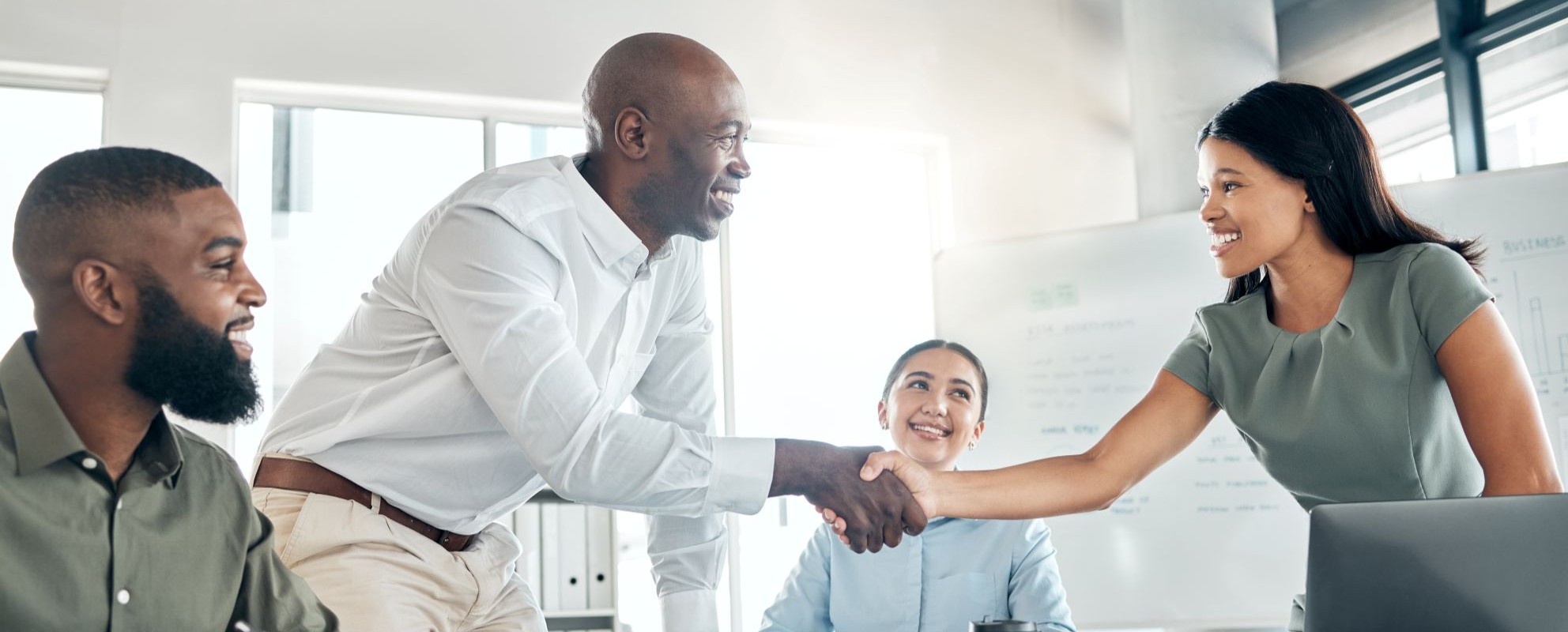 Leadership professionals in an office setting smiling and shaking hands after a positive interaction.
